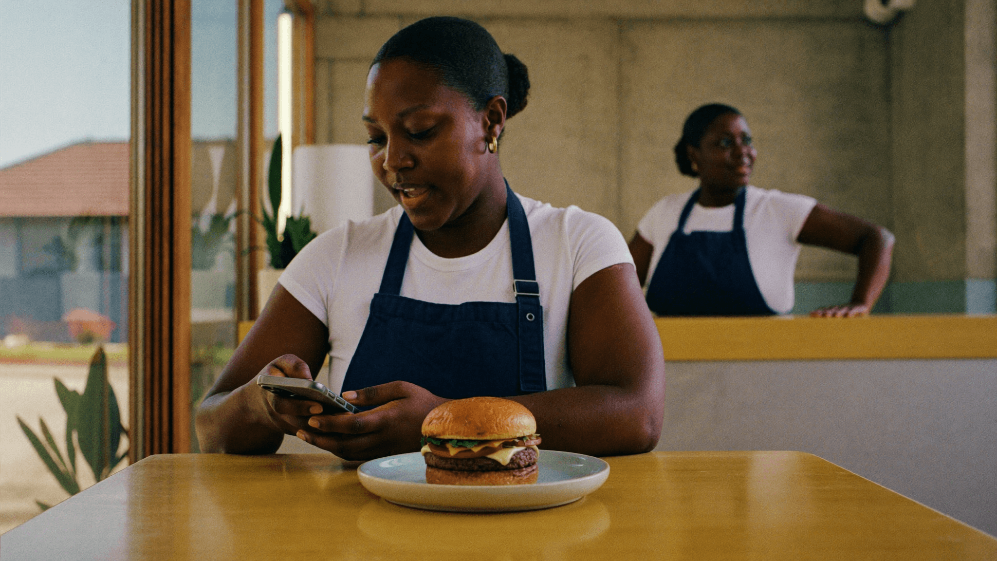 Cliente sentado à mesa de uma hamburgueria com o celular na mão, fazendo o pedido pelo WhatsApp